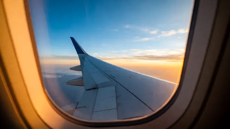 An airplane wing seen through a window against a sunset sky.