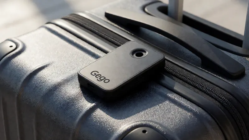 A close-up of a black, credit-card-sized Gego luggage tracker resting on the textured surface of a hard-shell suitcase.