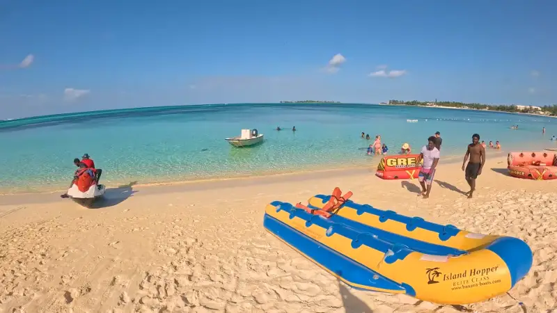 People relaxing on a sandy beach in Nassau with clear blue water and distant boats