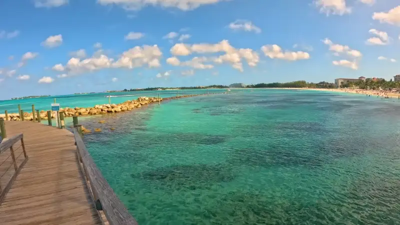 View from a wooden pier over vibrant turquoise water in Nassau, looking towards the coastline