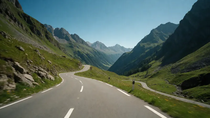 A winding alpine road with a dramatic mountain pass under a clear blue sky.
