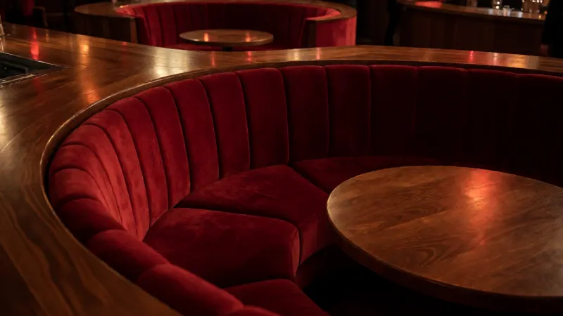 Plush red velvet seating in a dimly lit nightclub with a polished wooden bar.